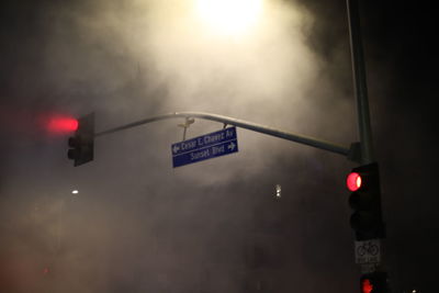 Illuminated road sign against sky at night