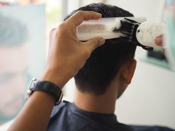 Cropped hand of barber cutting mid adult man hair