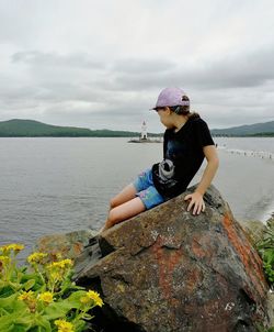 Man standing on rock by sea against sky