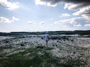 Rear view of man walking on landscape against sky