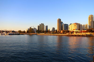 Buildings by river against clear sky in city