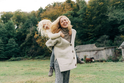 A little laughing girl is having fun with her mother sitting on her back.