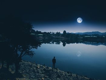 Rear view of man standing by lake against sky