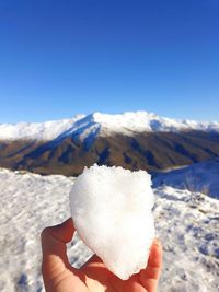 Person holding ice cream on snowcapped mountain against sky