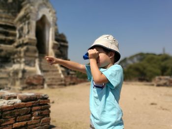 Boy gesturing while looking through binoculars at historic place