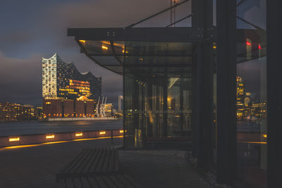 Illuminated street by buildings against sky at night