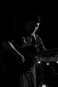 Man playing guitar against black background