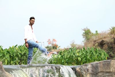 Young man sitting on field against clear sky