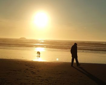 Silhouette people on beach against sky during sunset