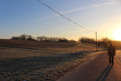 Rear view of man walking on road against sky during sunset