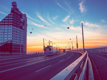 Vehicles on road against sky during sunset in city
