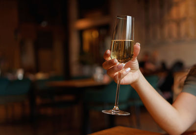 Female hand with french manicure holding a glass with wine or champagne on naturally blurred back