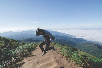 Side view of man climbing on mountain against sky