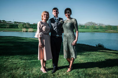 Full length of friends standing by lake against sky