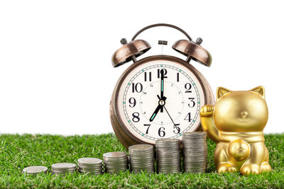 Close-up of maneki neko with coins and alarm clock on turf against white background