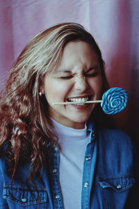 Close-up of young woman biting lollipop by curtain