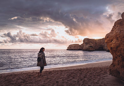 Woman standing on beach against sky during sunset