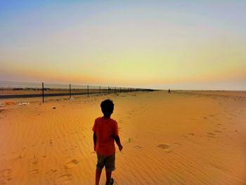 Rear view of boy in a beachagainst sky during sunset