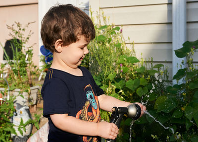 Little boy playing with a watering hose in the backyard