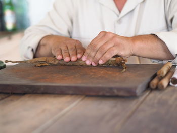 Midsection of man making cigars at table