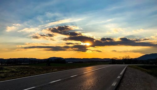 Road by landscape against sky during sunset