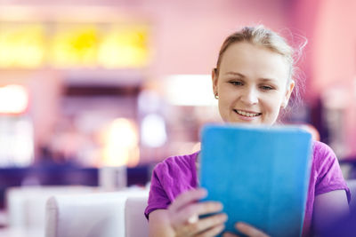 Happy young woman using digital tablet in restaurant