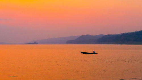 Silhouette person on boat in sea against orange sky