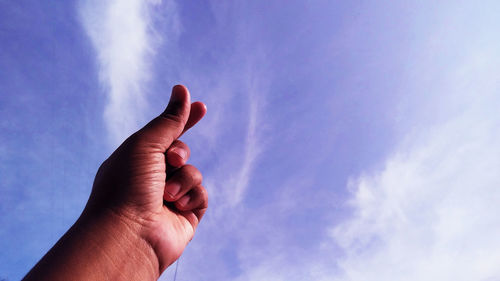 Low angle view of hand snapping finger against sky