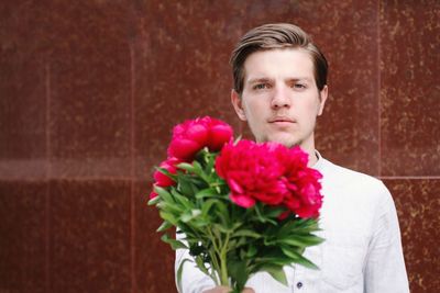 Portrait of handsome man standing against wall holding flower in hand