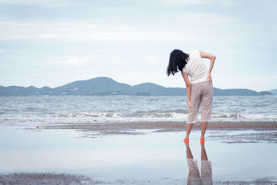 Rear view of woman standing by sea against sky