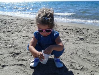 Girl wearing sunglasses while crouching on sand at beach
