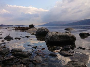 Rocks on shore by sea against sky