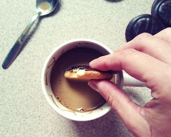 Cropped hand of woman dipping cookie in coffee