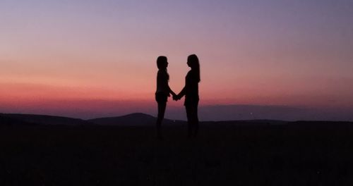 Silhouette men standing on shore against sky during sunset