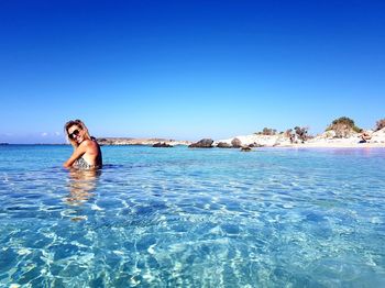 Woman wearing sunglasses swimming in sea against clear blue sky