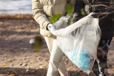 Midsection of female environmentalists holding plastic filled with garbage by lake