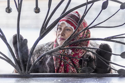 A slavic woman in a national colored scarf, a fur coat and  mittens on the porch of a wooden house