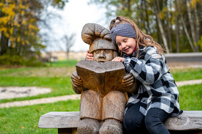 Cute girl sitting with sculpture at park