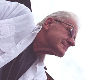 Low angle view of senior man wearing eyeglasses looking away while sitting against sky