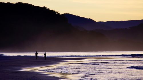 Silhouette people at beach against sky during sunset