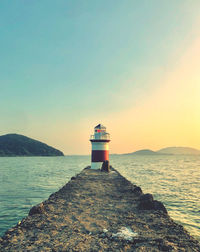 Lighthouse by sea against sky during sunset