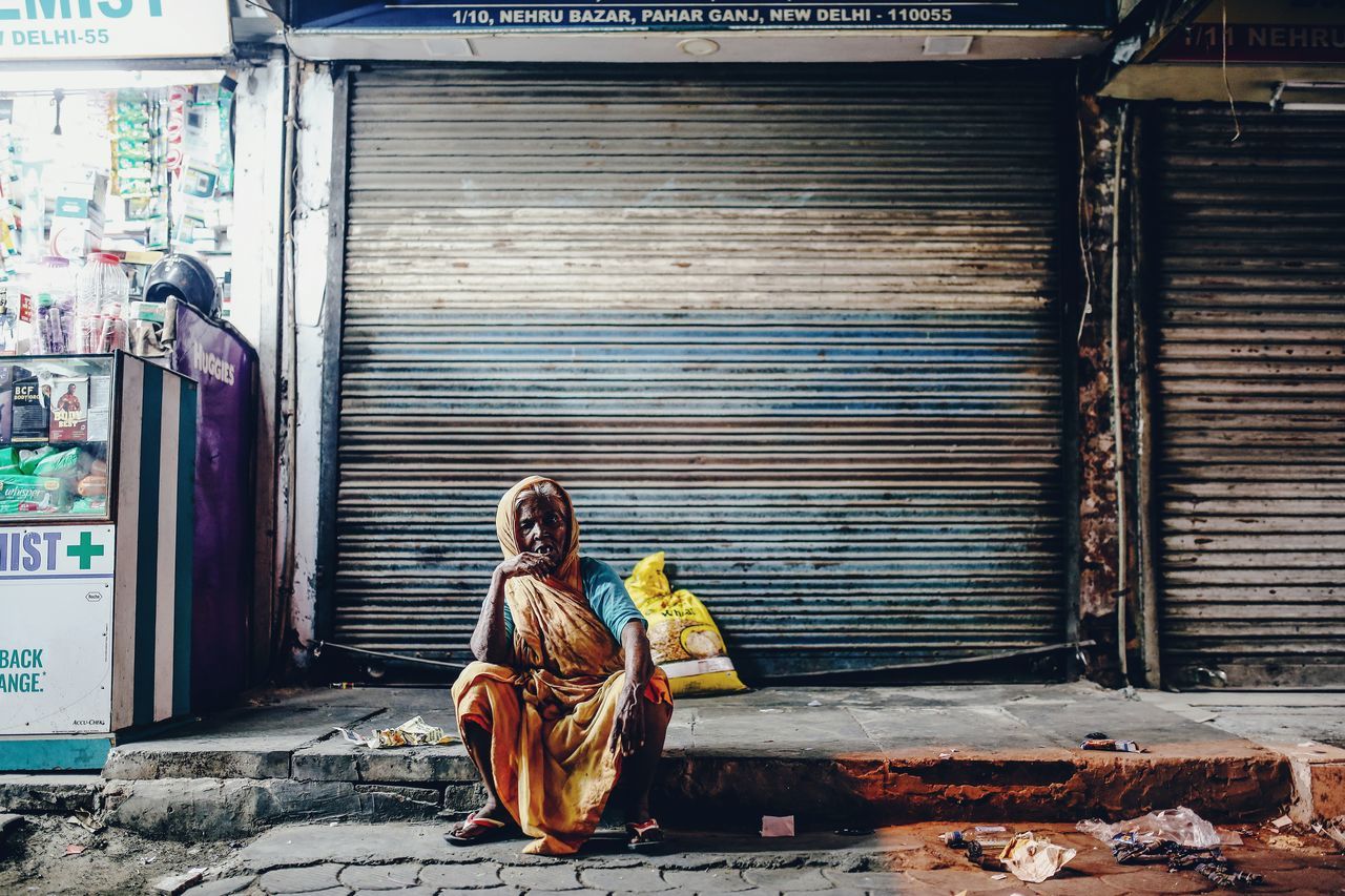 one person, full length, real people, sitting, shutter, architecture, traditional clothing, clothing, lifestyles, day, women, adult, young adult, built structure, side view, leisure activity, building exterior, casual clothing, store, outdoors, social issues, hopelessness