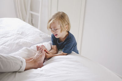 Smiling boy tickling grandmother's bare feet on bed at home