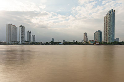 City at waterfront against cloudy sky