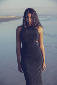 Young woman standing at sea shore against sky