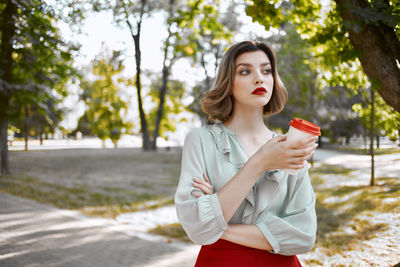 Beautiful young woman looking away while standing against trees