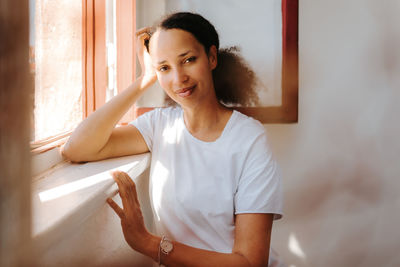 Portrait of young woman leaning against window at home