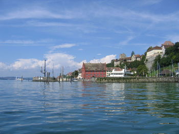 Sailboats in sea by buildings against sky