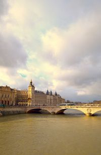 Arch bridge over river against cloudy sky