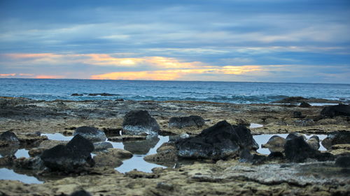 Rocks on beach against sky during sunset